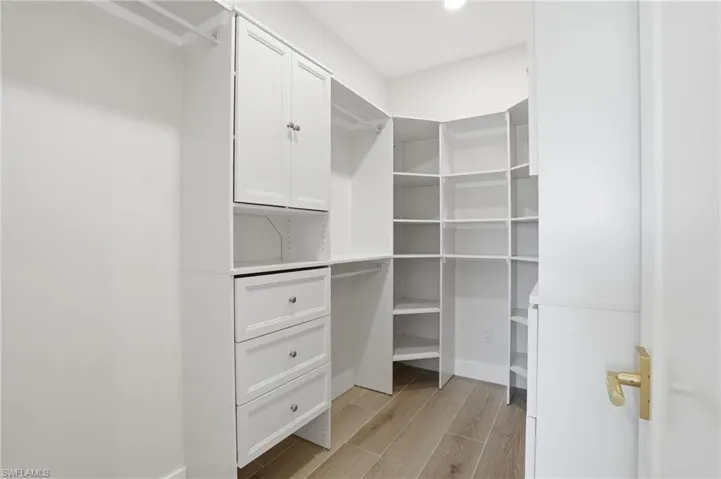 Custom closet featuring white cabinetry, drawers with silver-toned hardware, and extensive shelving - Virtually Edited Image