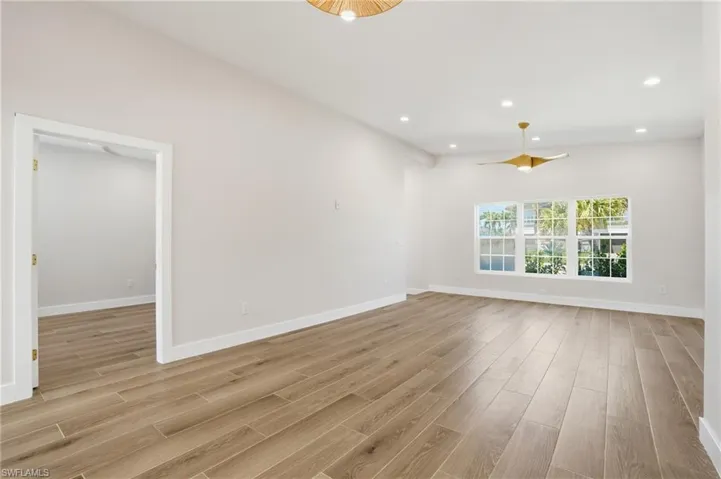 Spacious room featuring light wood-style flooring, white walls, and a contemporary ceiling fan - Virtually Edited Image