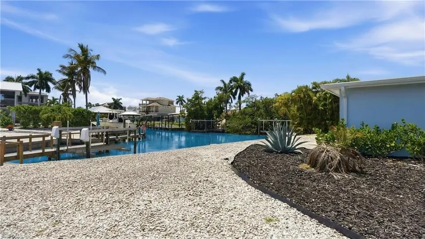 The property features a private dock with direct canal access, surrounded by lush landscaping and palm trees - Virtually Edited Image
