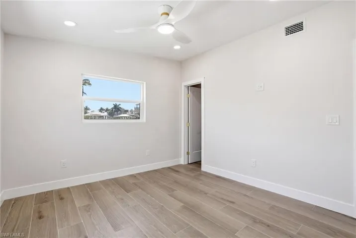 This room features light wood-look flooring, a window with a water view, and a ceiling fan with integrated lighting - Virtually Edited Image