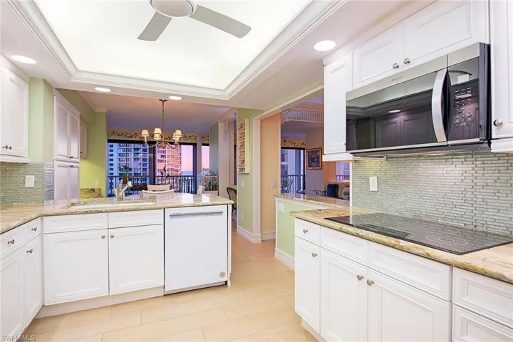 Kitchen with tasteful backsplash, a peninsula, stainless steel microwave, light stone counters, and a raised ceiling