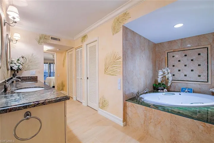 Bathroom featuring a closet, crown molding, double vanity, a jetted tub, and connected bathroom