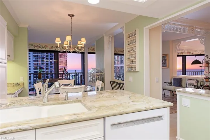 Kitchen with crown molding, dishwasher, light stone countertops, white cabinetry, and a chandelier