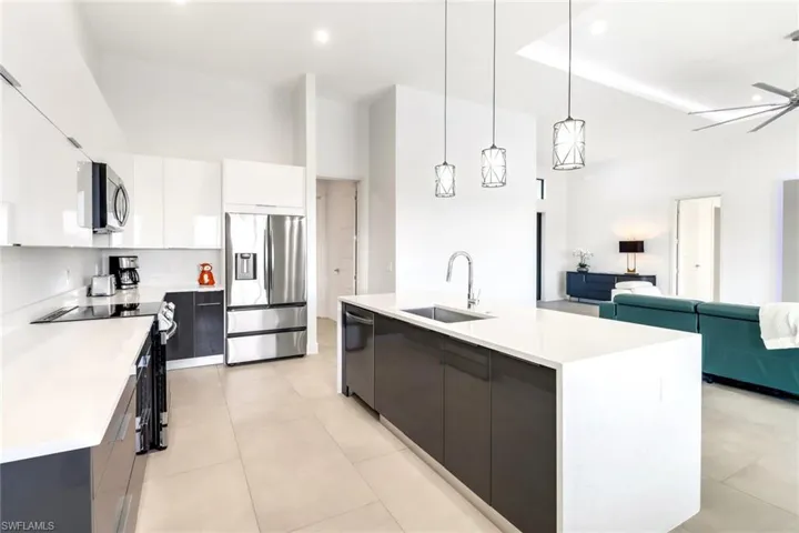 Kitchen featuring a center island with sink, appliances with stainless steel finishes, hanging light fixtures, white cabinetry, and a high ceiling