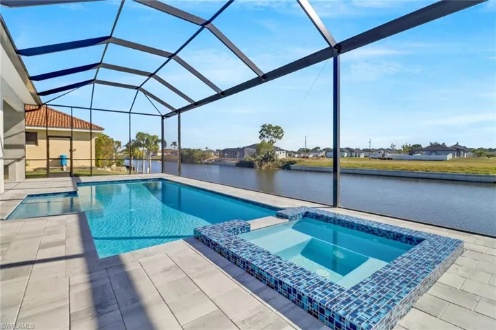 View of pool with a sunroom, a pool with connected hot tub, glass enclosure, a patio area, and a water view
