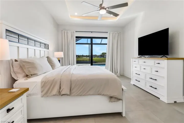 Bedroom featuring ceiling fan, a tray ceiling, light tile patterned flooring, and access to outside