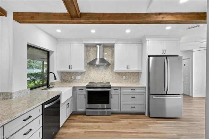 Kitchen with appliances with stainless steel finishes, light stone countertops, tasteful backsplash, recessed lighting, and wall chimney range hood