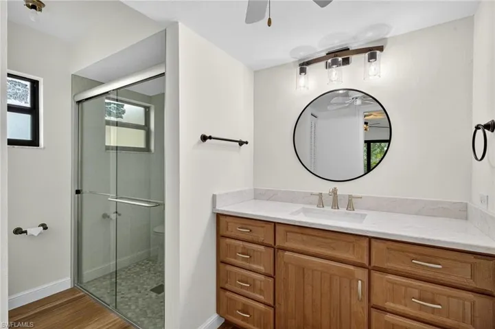 Full bathroom with a ceiling fan, a shower stall, vanity, and light wood finished floors