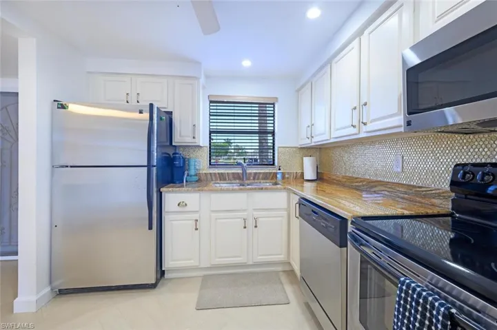 Kitchen featuring decorative backsplash, appliances with stainless steel finishes, light stone counters, and white cabinets--even a window over the sink!