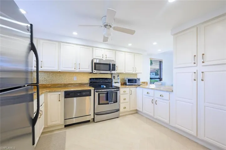 Kitchen with appliances with stainless steel finishes, ample white cabinets, ceiling fan, light parquet flooring, and light stone counters.