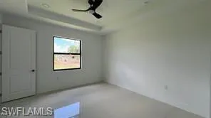 Spacious room featuring light-toned flooring, white walls, and a tray ceiling with a ceiling fan