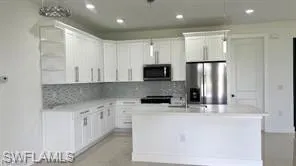 Kitchen featuring white cabinetry with silver-tone hardware, a mosaic tile backsplash, built-in stainless steel appliances, and a central island with integrated sink