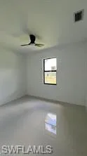 Spacious interior room featuring light-colored tile flooring, a window with dark trim, and a ceiling fan