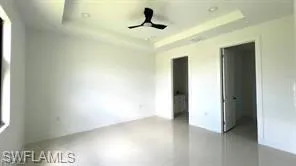 Spacious room featuring light-toned tile flooring, a tray ceiling with recessed lighting, and a dark-toned ceiling fan