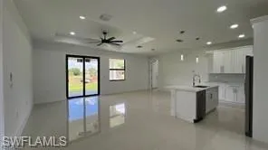 Open-concept kitchen and living area featuring a kitchen island with sink, white cabinetry, stainless steel appliances, and sleek tile flooring