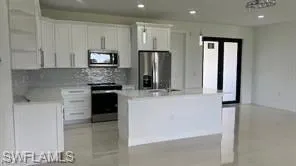 Modern kitchen featuring white cabinetry, stainless steel appliances, a center island with sink, and light-toned flooring