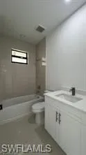 Bathroom featuring a contemporary white vanity with a single sink, an integrated bathtub and shower, and neutral-toned wall tiling
