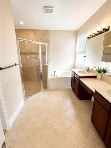 Spacious bathroom featuring diagonal tile flooring, a glass-enclosed shower with tiled walls and decorative banding, a separate soaking tub, and a dual vanity with dark wood cabinetry and light countertops