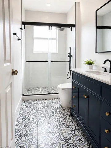 Bathroom on the second floor featuring decorative floor tiling, a dark blue vanity with brass hardware, a glass-enclosed shower with matte black fixtures, a window within the shower, and a frameless mirror