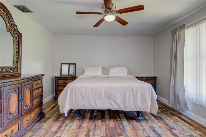 Bedroom with wood finished floors, ceiling fan, baseboards, and visible vents