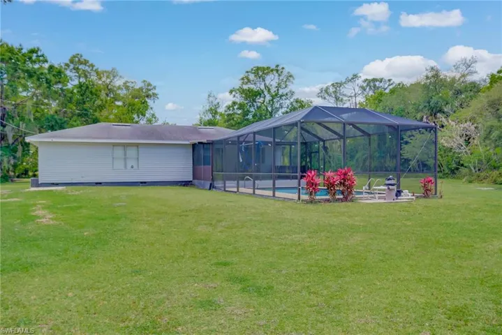 Back of house with crawl space, a yard, glass enclosure, a patio, and an outdoor pool