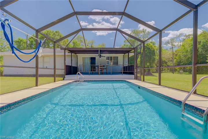 Outdoor pool featuring a yard, ceiling fan, glass enclosure, and a patio area