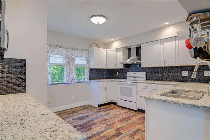 Kitchen featuring wall chimney exhaust hood, a sink, white electric stove, and decorative backsplash