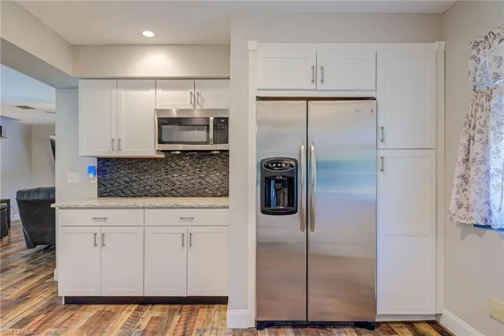 Kitchen with light stone counters, white cabinetry, decorative backsplash, appliances with stainless steel finishes, and wood finished floors