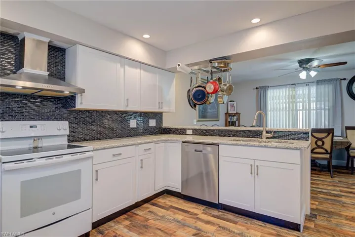 Kitchen with dishwasher, a sink, wall chimney range hood, a peninsula, and white electric range