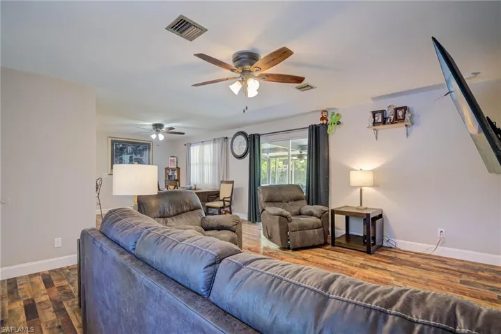 Living area with dark wood-type flooring, visible vents, baseboards, and a ceiling fan