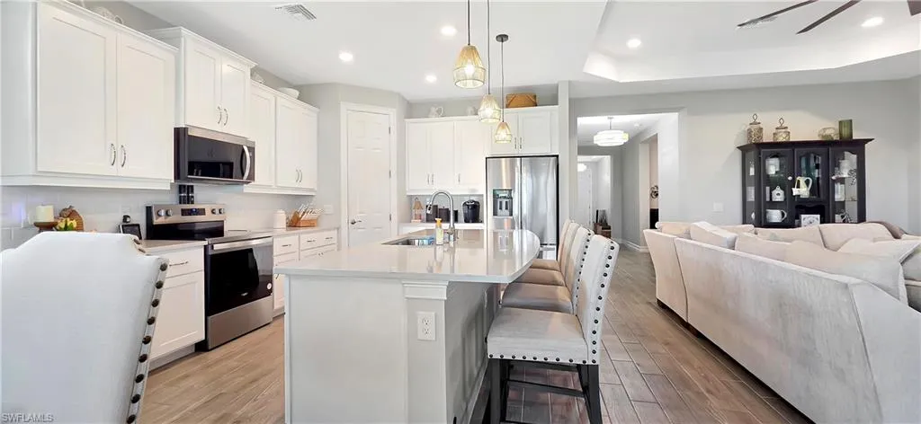 Open-concept living area featuring plank ceramic floors, a tray ceiling with recessed lighting and a ceiling fan, and sliding glass doors to the exterior