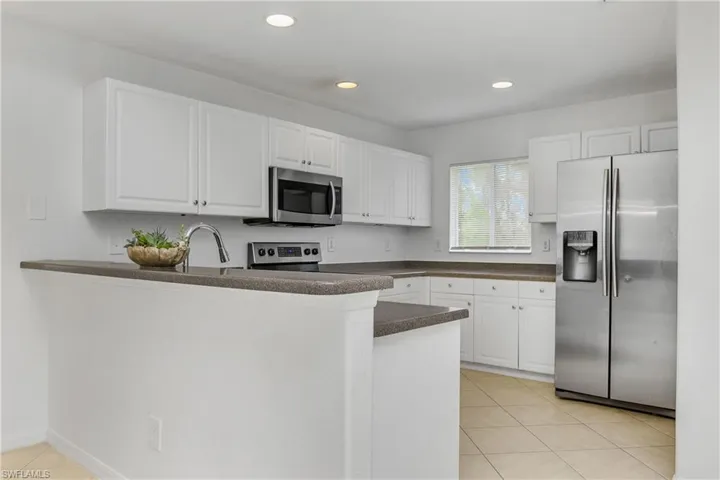 Kitchen with appliances with stainless steel finishes, light tile patterned flooring, white cabinetry, and kitchen peninsula