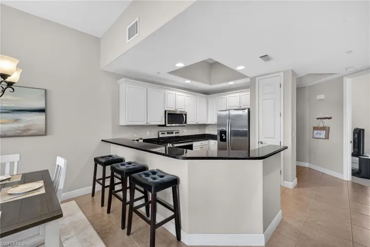 Kitchen with stainless steel appliances, a peninsula, dark stone countertops, white cabinetry, and light tile patterned flooring