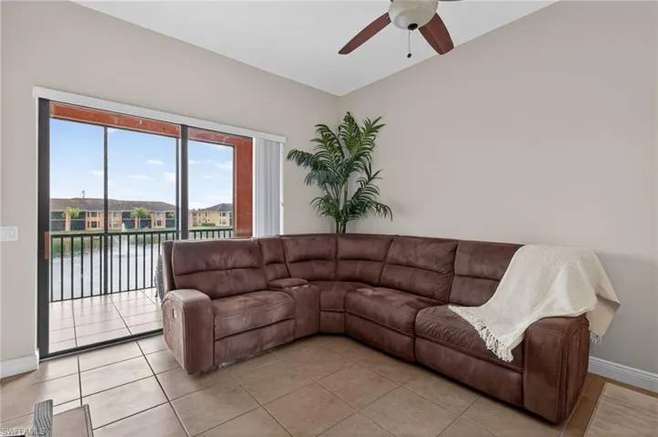 Living area featuring ceiling fan, light tile patterned floors, lofted ceiling, and a residential view