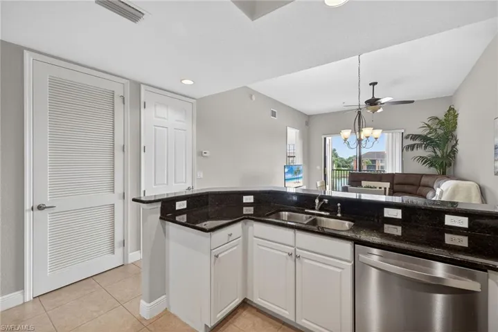 Kitchen featuring white cabinets, dark stone countertops, stainless steel dishwasher, open floor plan, and a ceiling fan