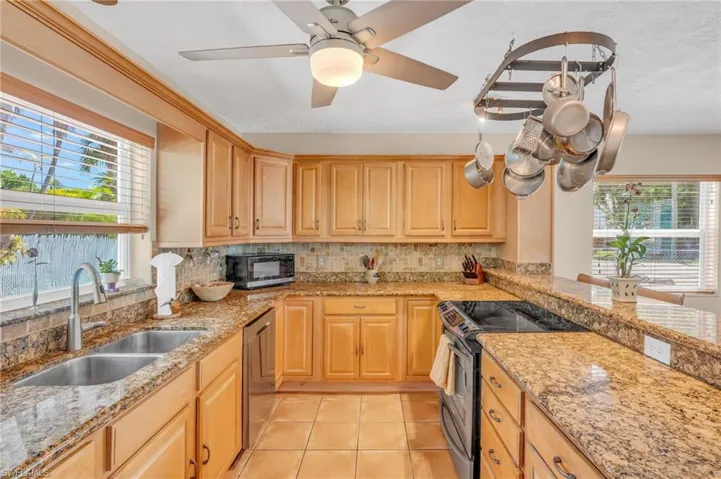 Kitchen featuring sink, decorative backsplash, stainless steel appliances, light stone countertops, and ceiling fan