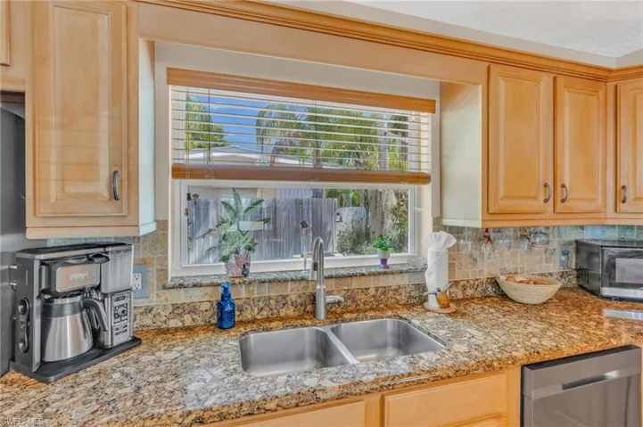 Kitchen with light stone counters, sink, decorative backsplash, stainless steel appliances, and light brown cabinets
