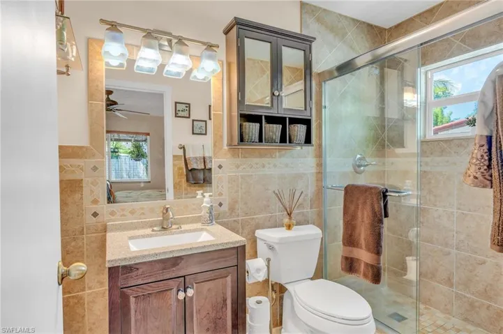 Bathroom with tile walls, a shower with shower door, vanity, ceiling fan, and toilet