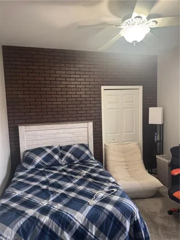 Carpeted bedroom with ceiling fan, brick wall, and a closet