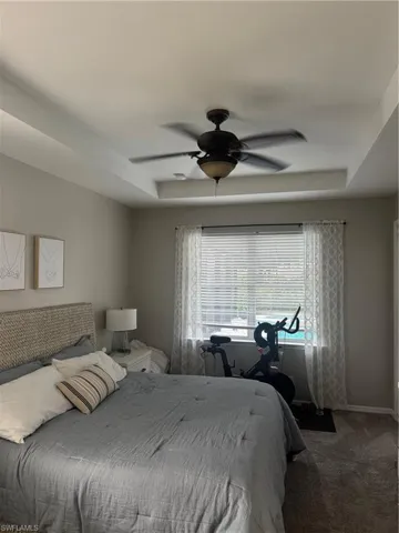 Bedroom featuring a raised ceiling, carpet flooring, and a ceiling fan