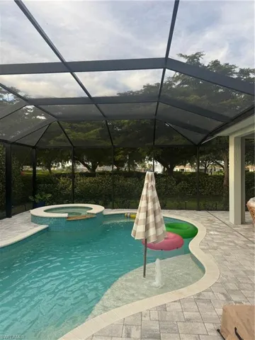 View of pool featuring a sunroom, a pool with connected hot tub, glass enclosure, and a patio