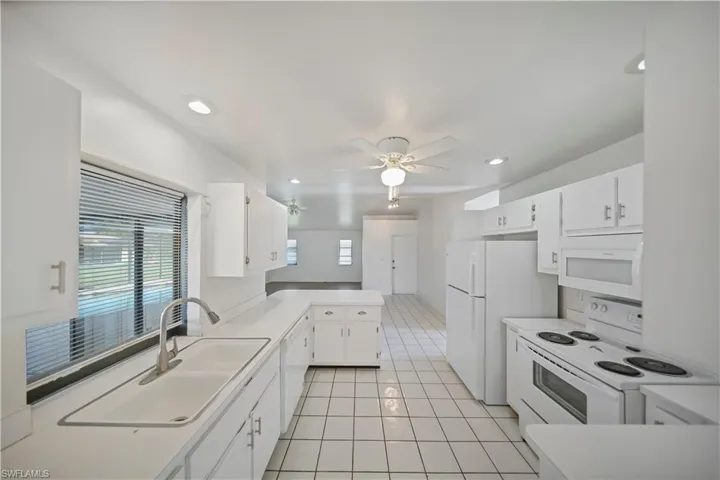 Bright kitchen featuring white cabinetry, a dual-basin sink with a gooseneck faucet, white appliances, recessed lighting, and a ceiling fan