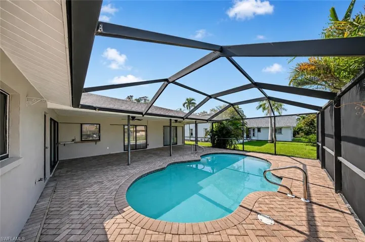 Screened-in pool deck featuring a freeform swimming pool, brick paver patio, and multiple access points to the residence