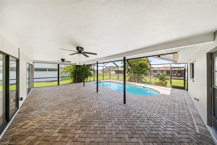 Screened lanai featuring a curved swimming pool and herringbone brick paver flooring