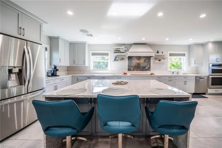 Kitchen featuring open shelves, premium range hood, a breakfast bar, and stainless steel appliances