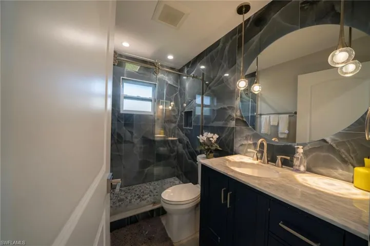Bathroom featuring a marble finish shower, visible vents, toilet, vanity, and tile walls