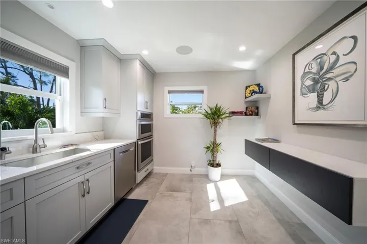 Kitchen with light countertops, stainless steel dishwasher, gray cabinets, and a sink