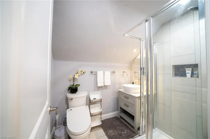 Full bath with lofted ceiling, toilet, vanity, baseboards, and a stall shower