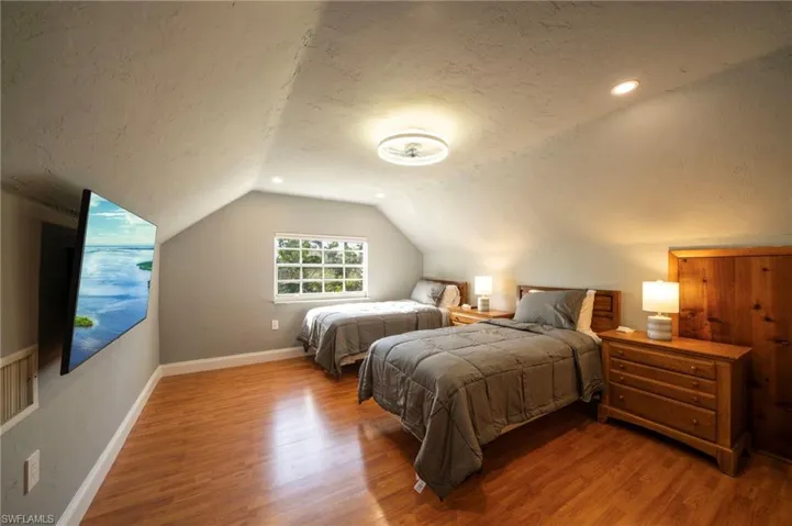 Bedroom with a textured ceiling, baseboards, wood finished floors, and lofted ceiling
