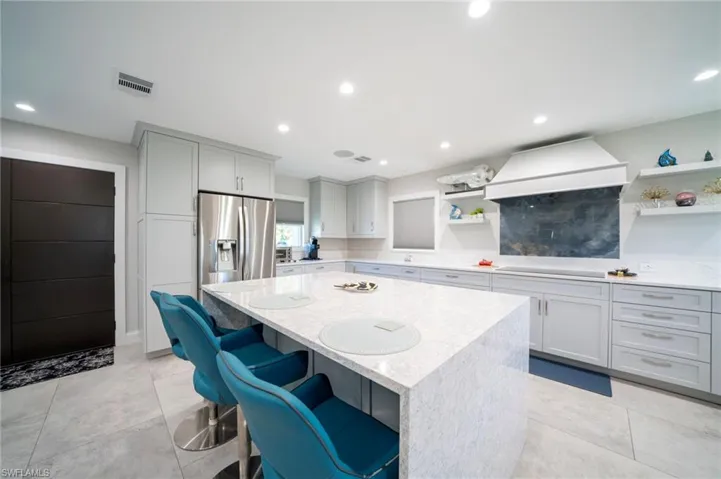 Kitchen featuring open shelves, visible vents, a kitchen island, stainless steel fridge, and premium range hood